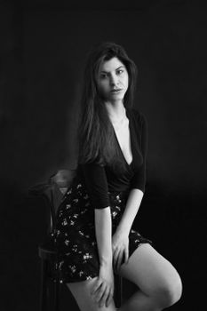 Black and white portrait of a woman seated on a wooden chair in a studio setting.