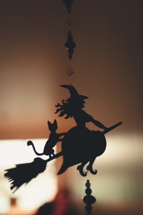 Silhouette of creative decoration of witch and cat flying on besom hanging in dark room