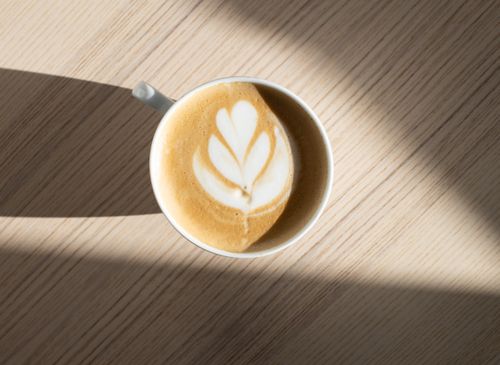 Free Top view of ceramic mug of tasty coffee with floral decoration on foam on table with shadows Stock Photo