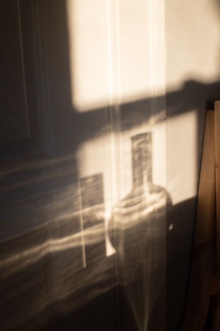 Wall with gentle shadows of glass flasks of different shape in sunlight in daytime