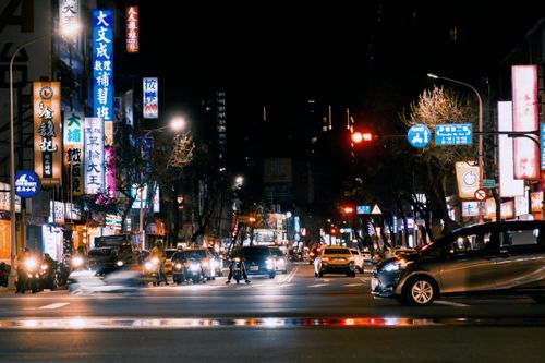 Free A bustling city street at night filled with illuminated signs, cars, and pedestrians. Stock Photo