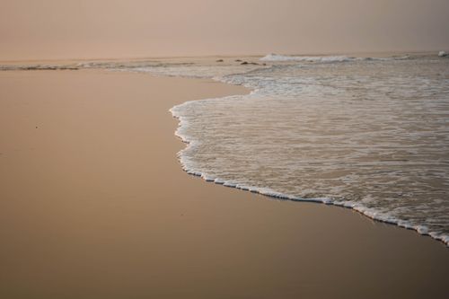 Free Tranquil view of gentle ocean waves meeting the sandy shore at dusk with a calming atmosphere. Stock Photo