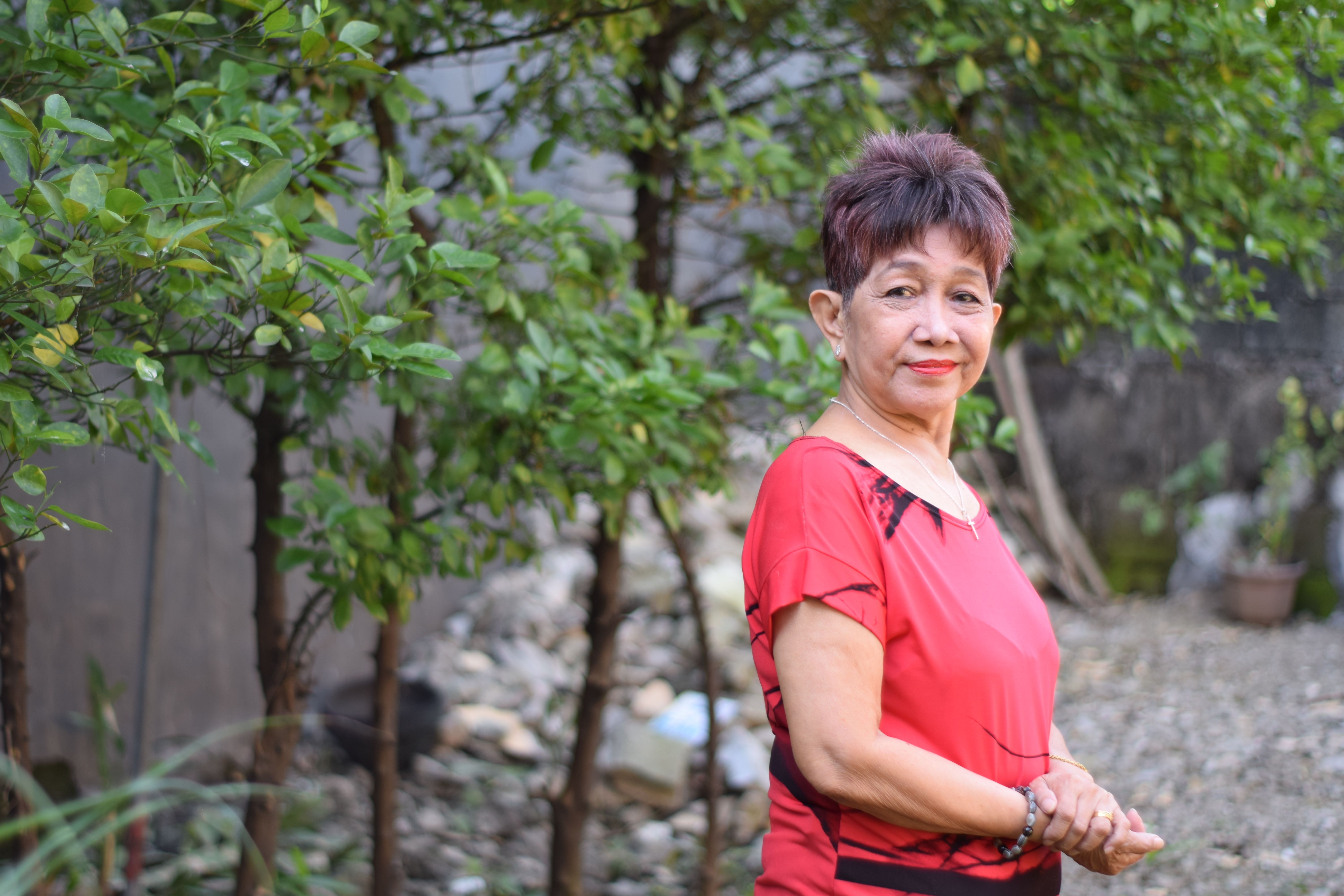 Senior woman standing in garden with green foliage.