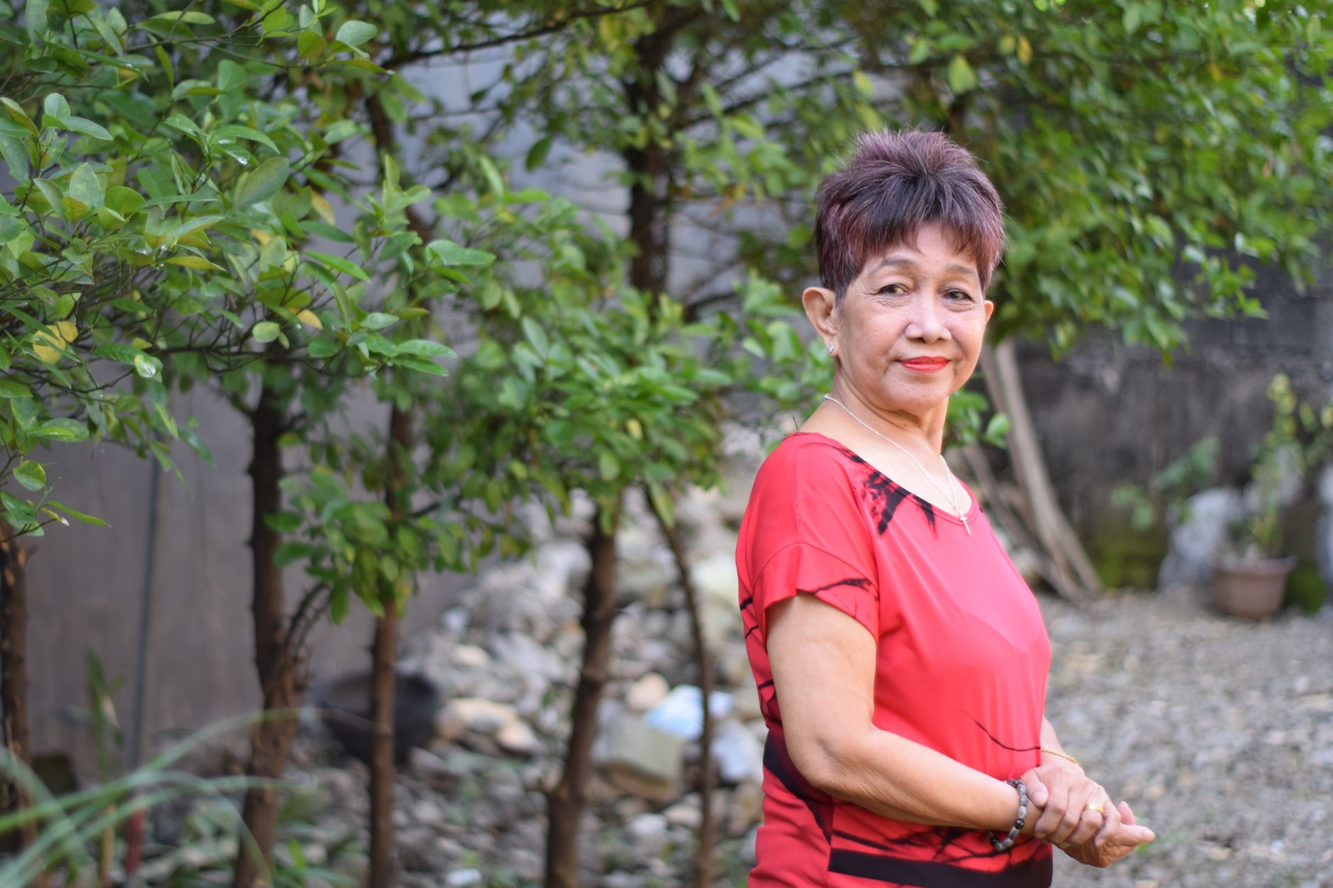 Senior woman standing in garden with green foliage.