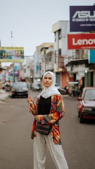 Portrait of a young woman in a hijab standing on a bustling street in Jawa Barat, Indonesia, captured during the day. - Fotografer Sidoarjo