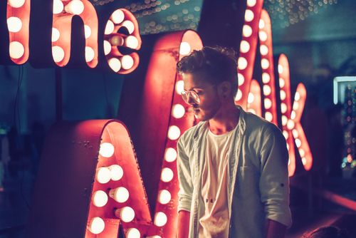 Free A stylish man stands near illuminated lettering in a vibrant nightclub setting, exuding a sense of nightlife glamour. Stock Photo