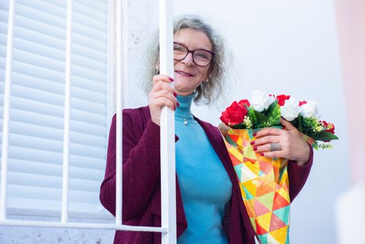 Smiling elderly woman holding a vibrant bouquet near a doorway.