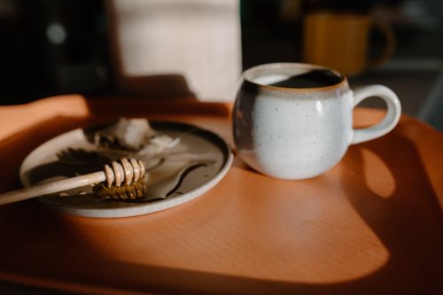 Free A cozy still life with a rustic tea mug and honey dip, bathed in warm sunlight. Stock Photo