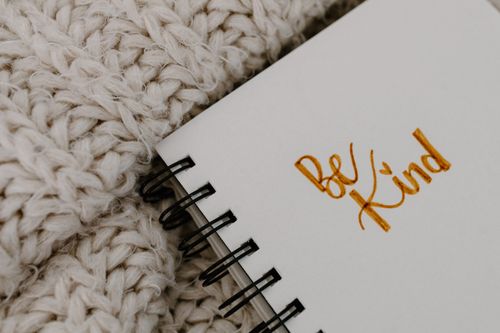 Free Handwritten 'Be Kind' affirmation on a notebook with a warm knitted blanket background. Stock Photo