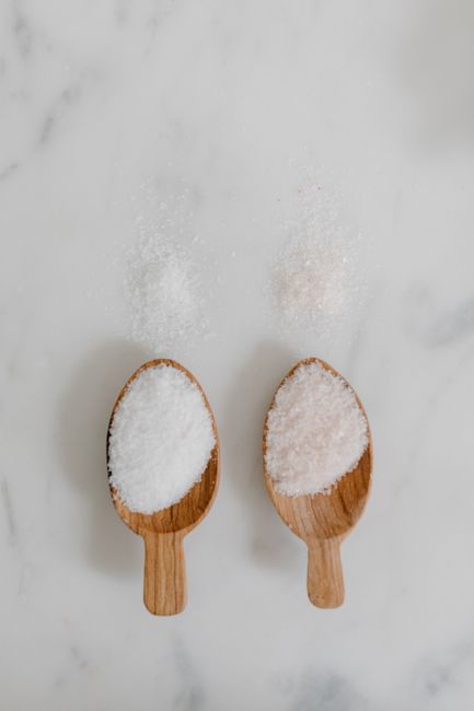 Fotomural Dos cucharas de madera con sales de baño rosas y blancas sobre una superficie de mármol.