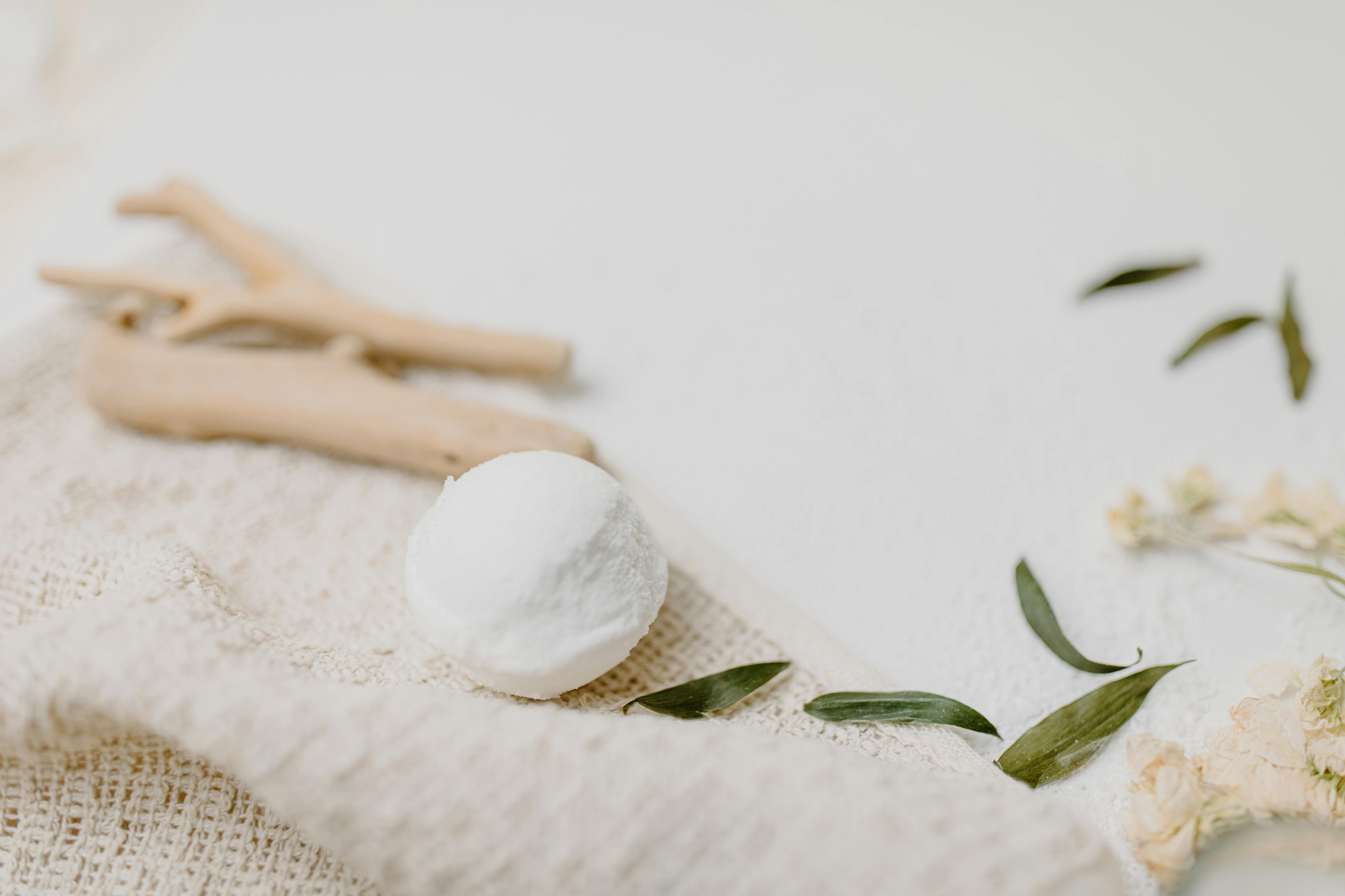 A serene flat lay image featuring a bath bomb, driftwood, and leaves on a textured fabric, evoking relaxation.