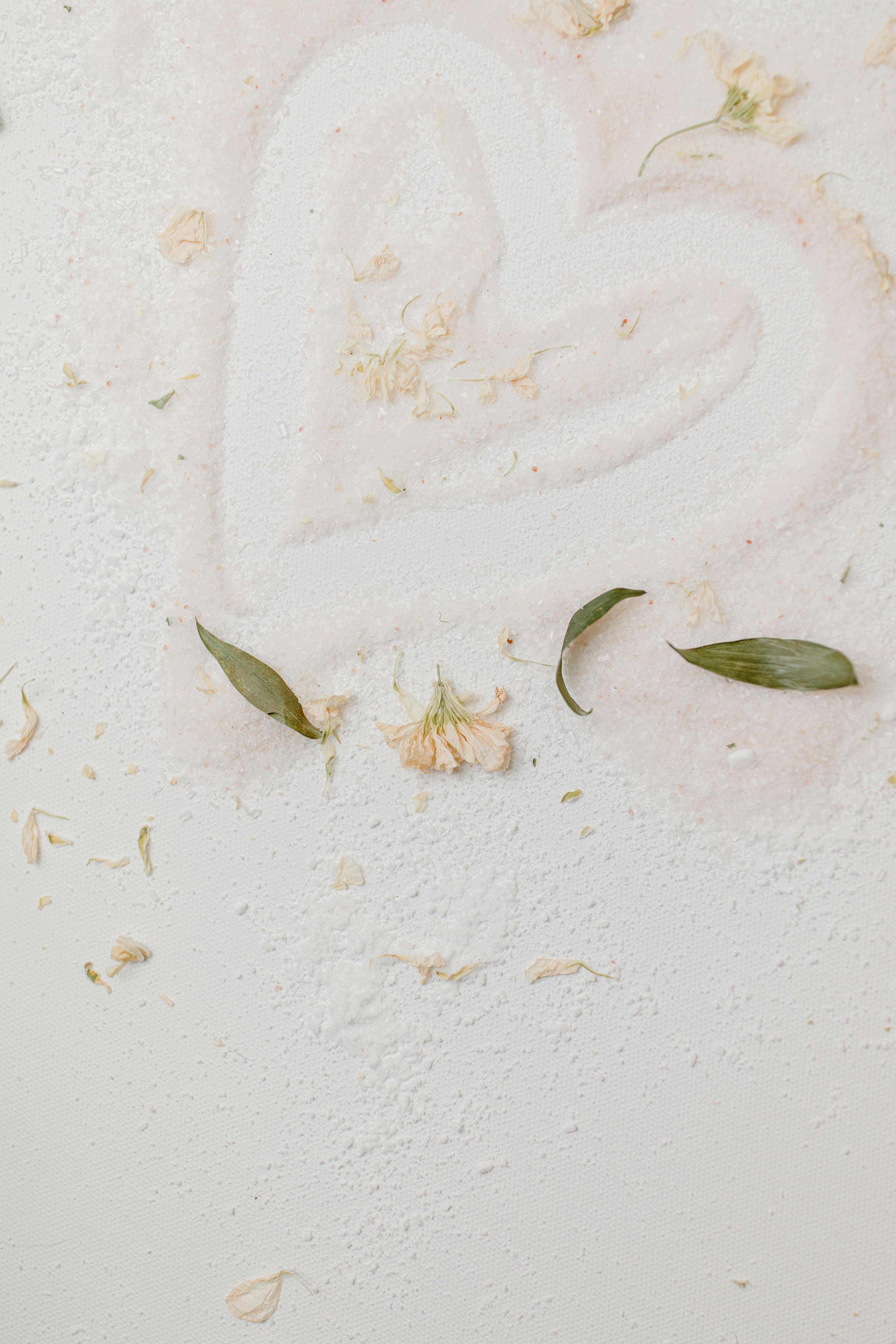 A heart shape drawn in sand accentuated with leaves and petals, evoking romance and nature.
