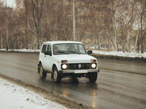 A vintage white SUV navigates a snowy road in winter, portraying a classic automotive scene.