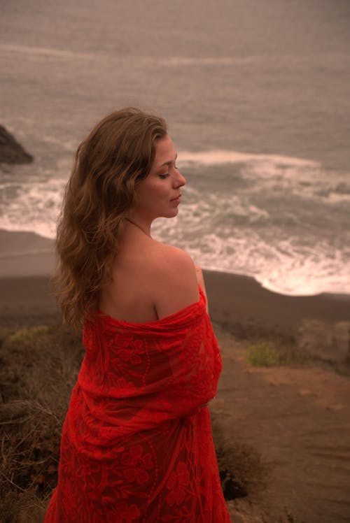 High angle back view of dreamy female with bare shoulders and closed eyes standing on seashore