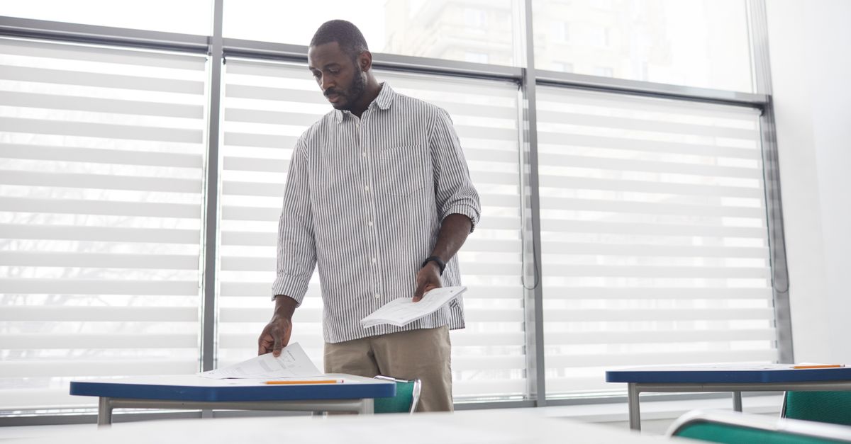 exhausted teacher in empty classroom with stacks of papers