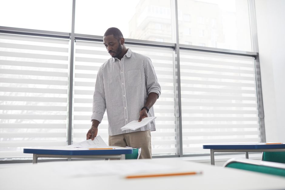 Educator sorting tests in a bright, contemporary indoor classroom setting. Educator sorting tests in a bright, contemporary indoor classroom setting.