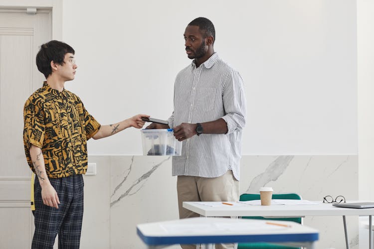 A Young Man Giving His Phone To His Teacher