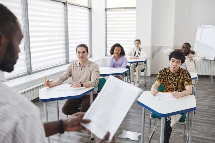 Students Sitting Inside The Classroom While Looking At Their Teacher