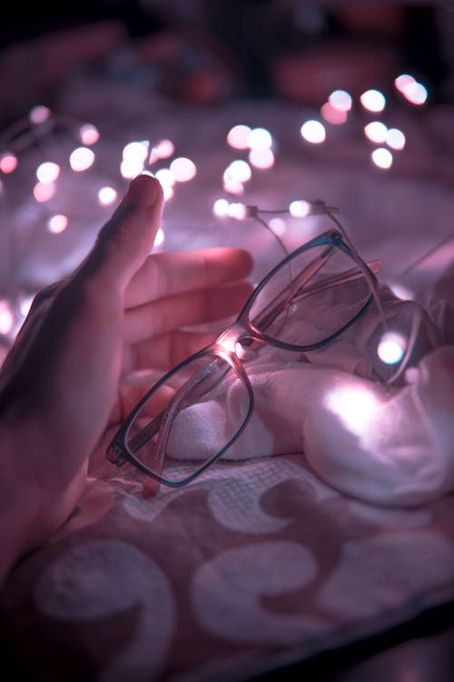 Free Black Frame Eyeglasses and White String Lights in White Textile Stock Photo