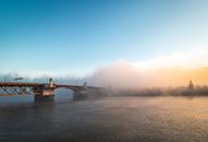 Magnificent scenery of famous Burnside Bridge crossing rippling river and hidden under fog against colorful sunset sky