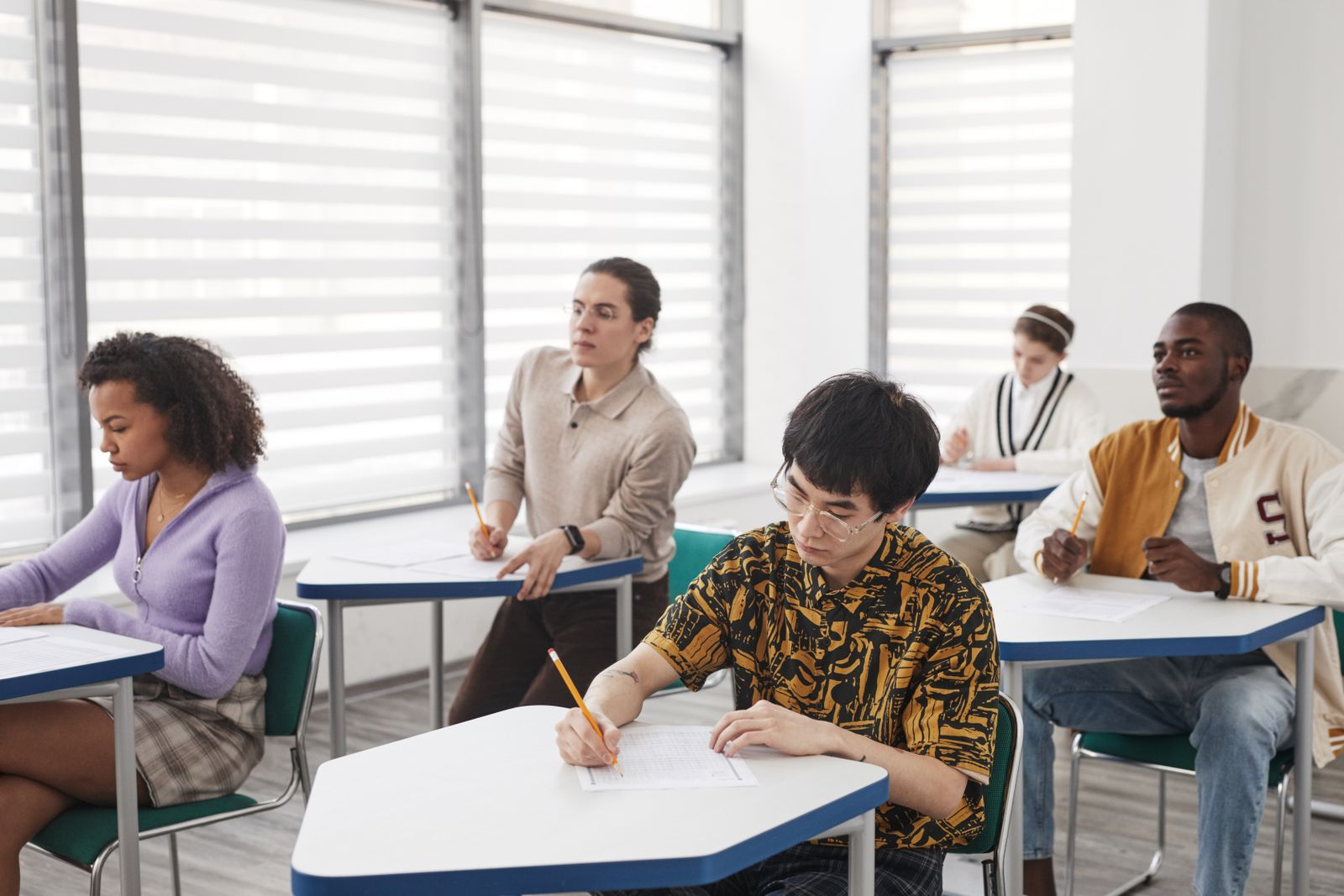 Students writing examination papers at desks in a classroom