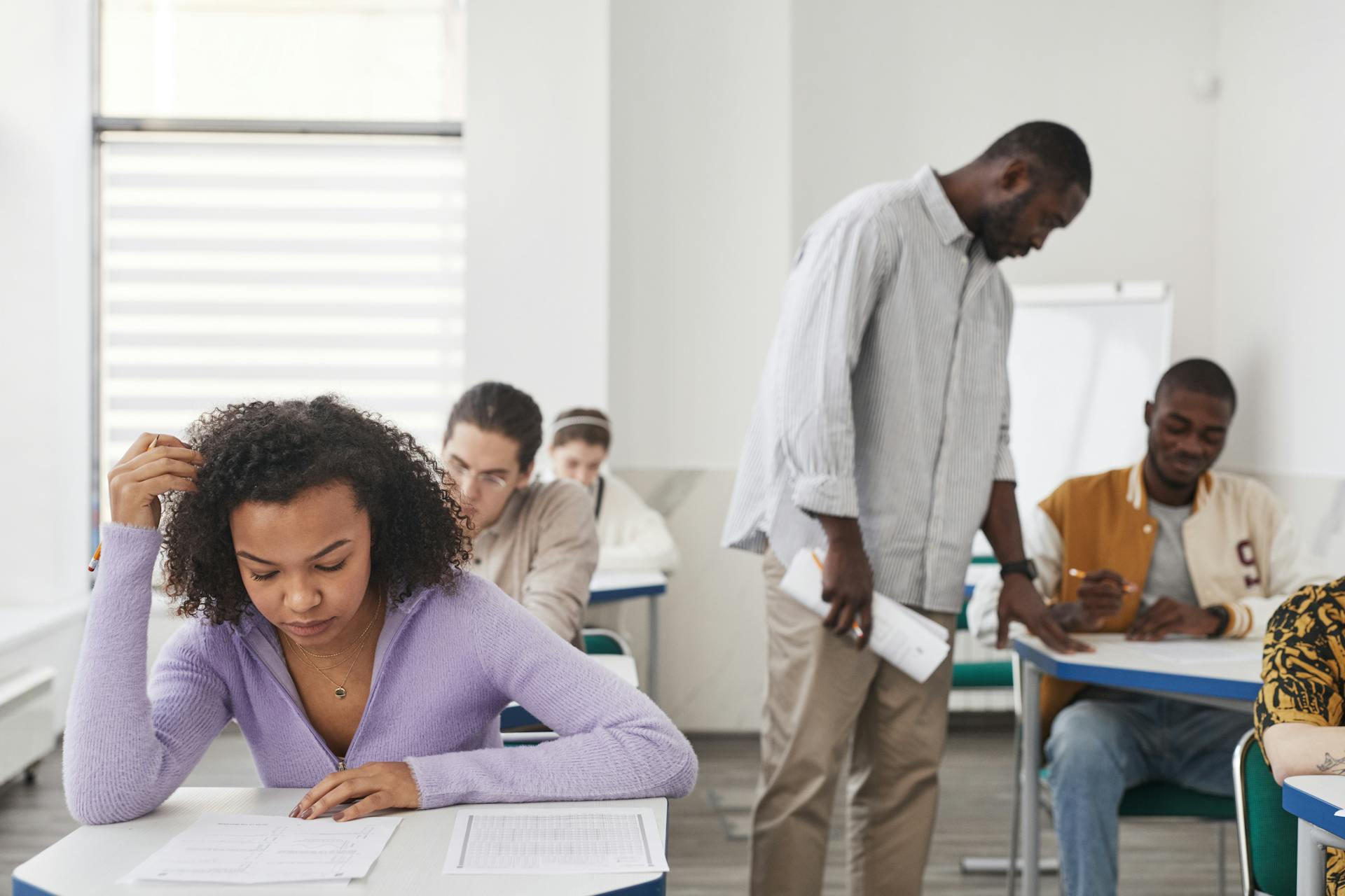 A diverse group of students taking an exam in a modern classroom with a teacher supervising.