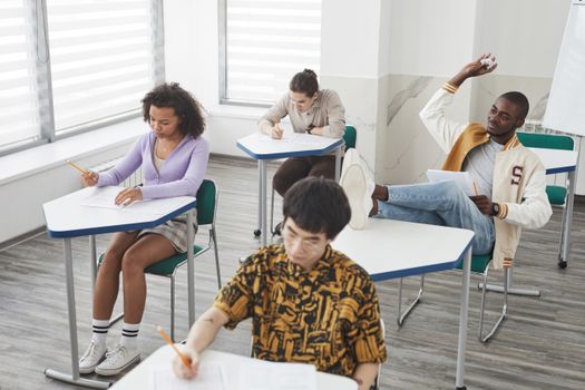Four diverse college students taking exams in a modern classroom setting, emphasizing concentration and diversity.