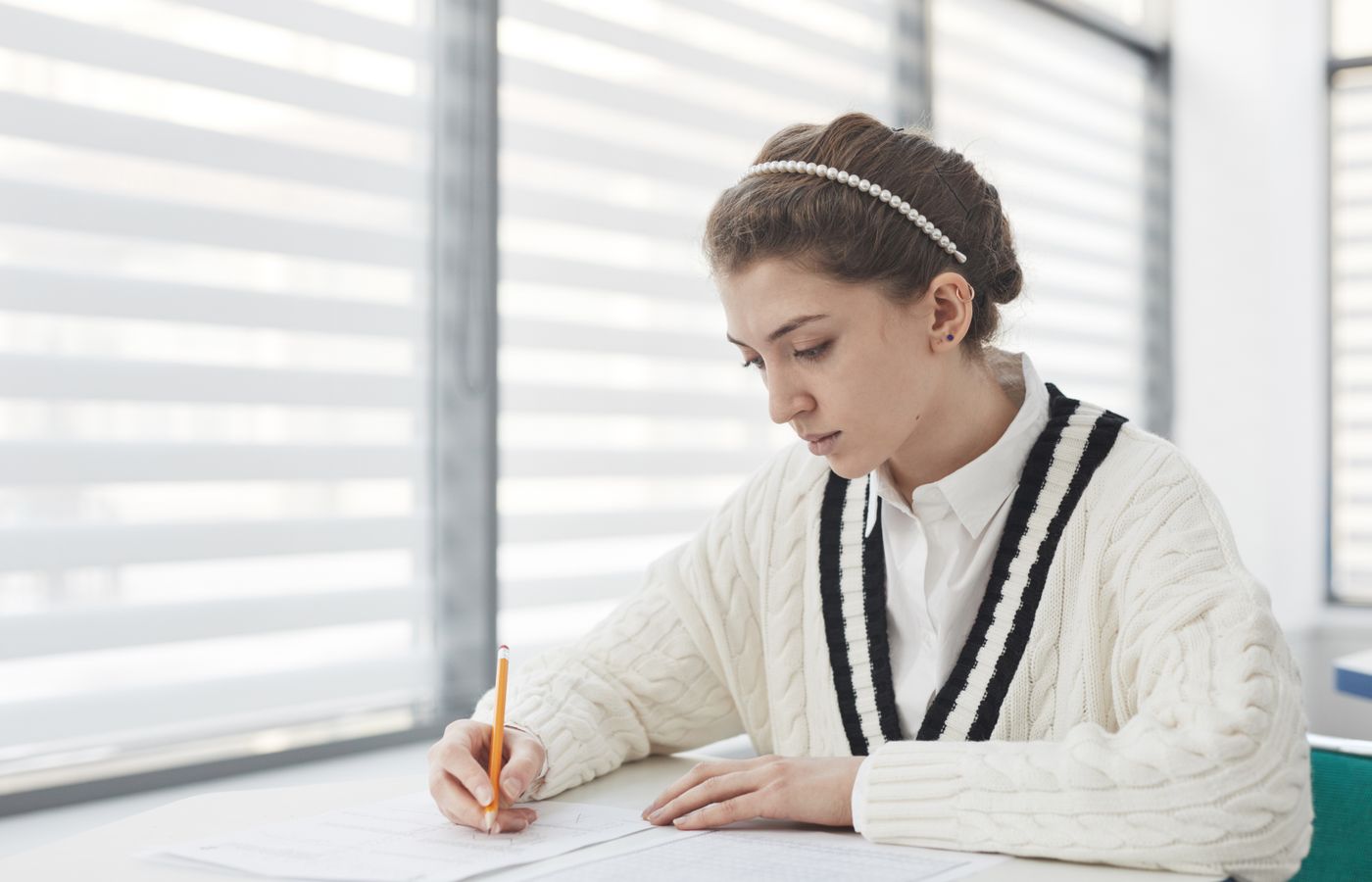 A student intensely focused on writing during an exam in a bright classroom setting.