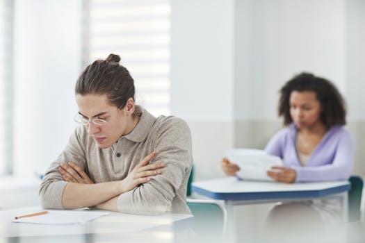 Students concentrating on an exam in a bright, indoor classroom setting.