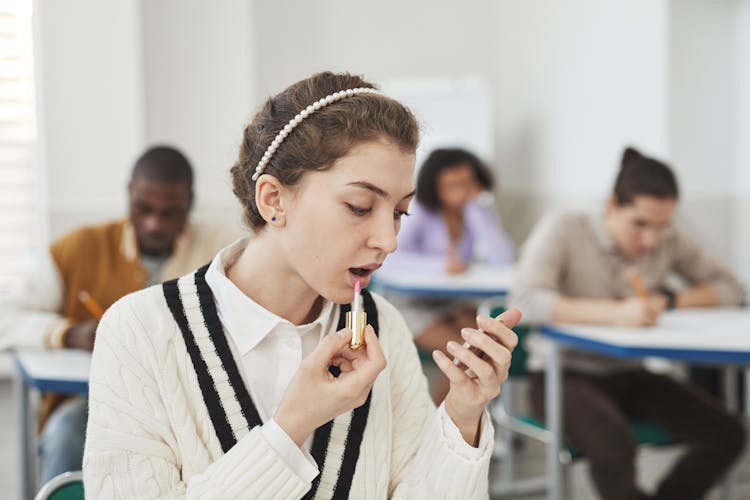 A Woman Applying Lipstick In A Classroom