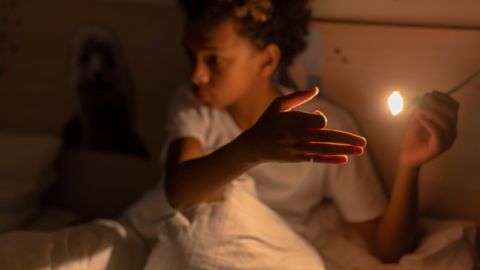 A young boy engaging with a light source in a dimly lit bedroom, creating a playful atmosphere.
