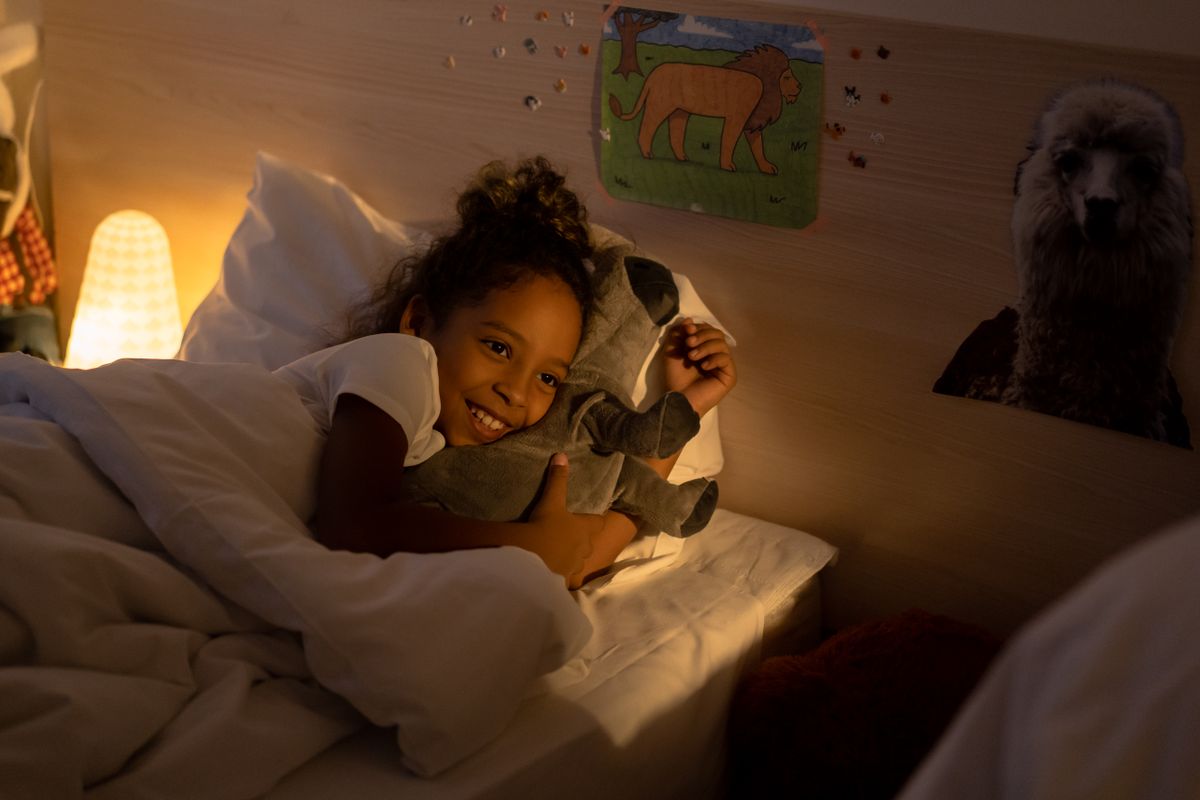 Child smiling while cuddling a soft toy in bed