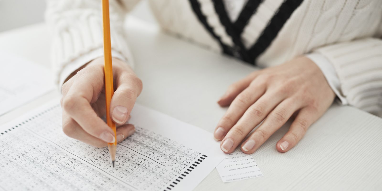 A student writing answers on a multiple-choice exam sheet at a desk.