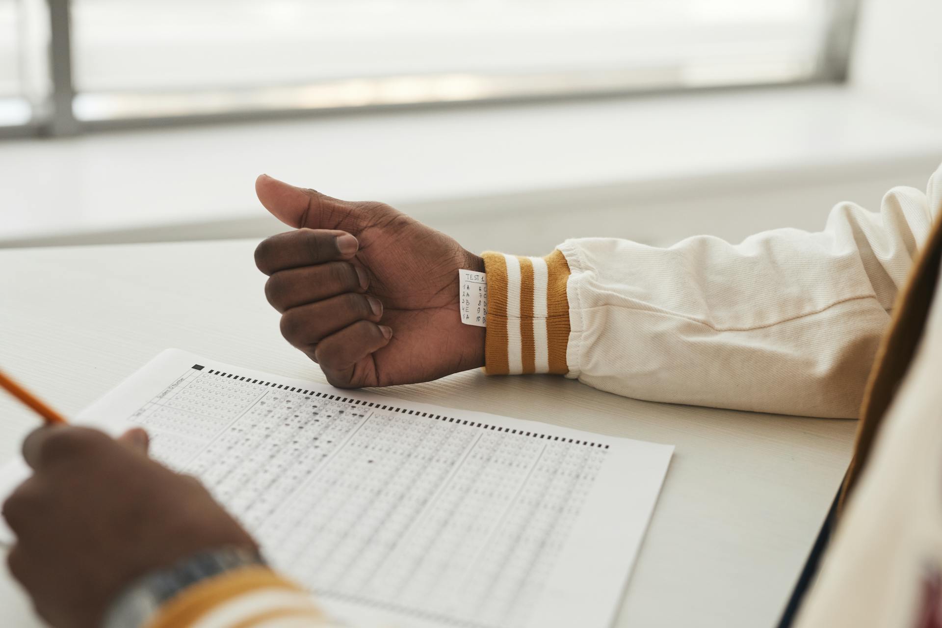 Close-up of a student cheating in an exam by hiding notes under a sleeve during a test.