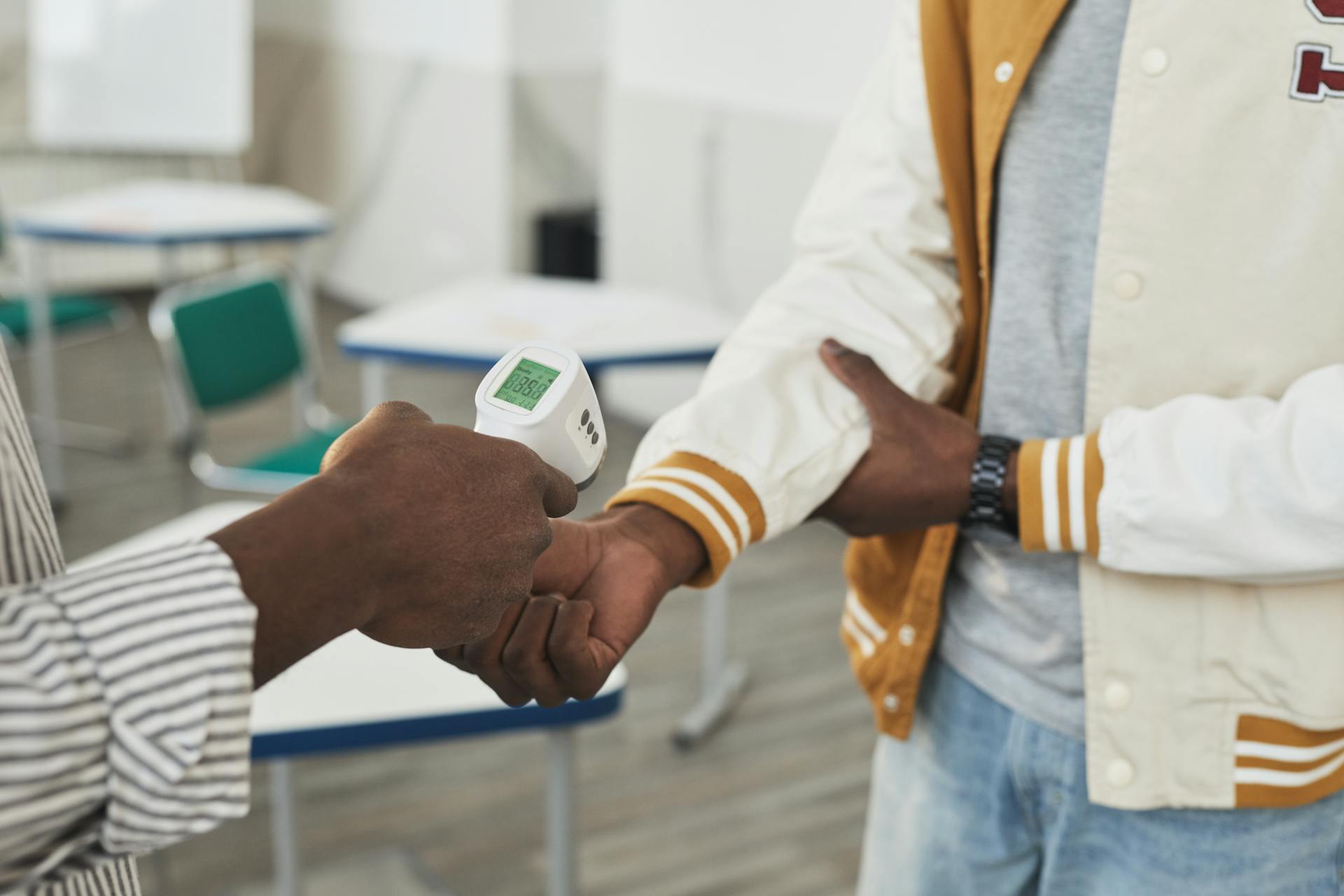 A contactless temperature check being conducted in an indoor classroom setting for safety measures.