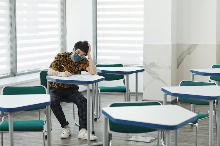 A Man Sitting Inside The Classroom While Wearing Face Mask