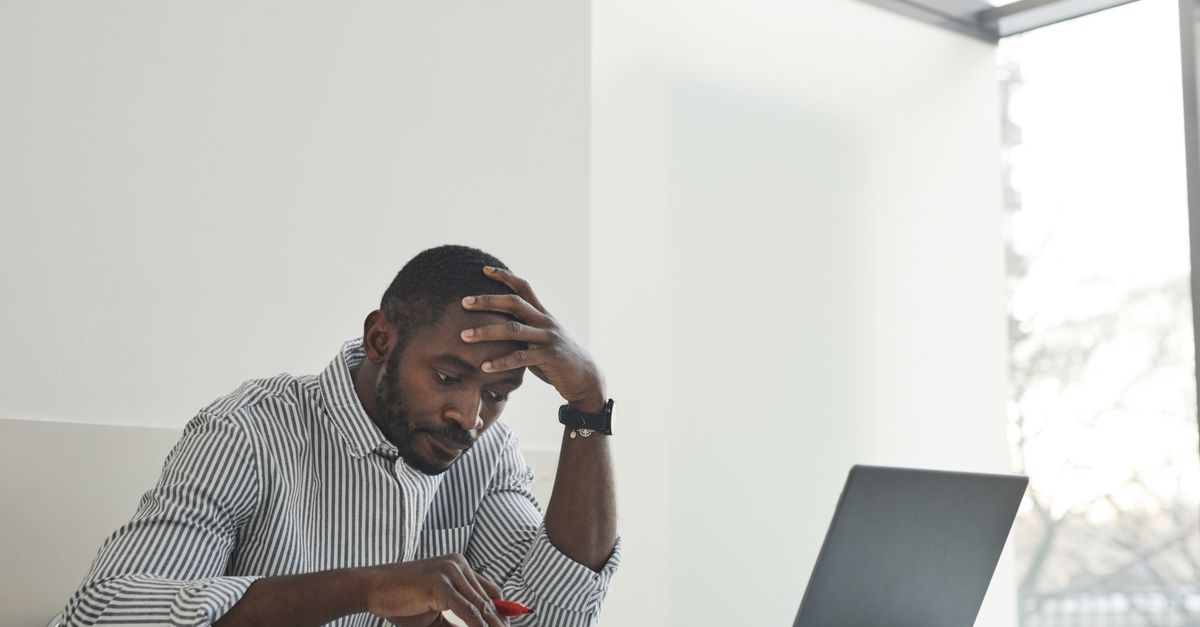 Person sitting at a desk with head in hand, looking at a laptop screen