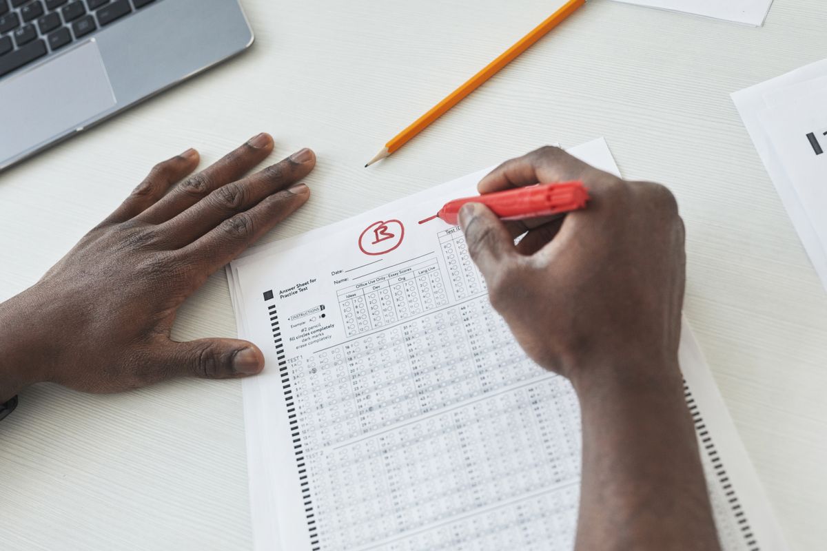 Close-up of a teacher grading multiple choice exams with a red pen on a desk