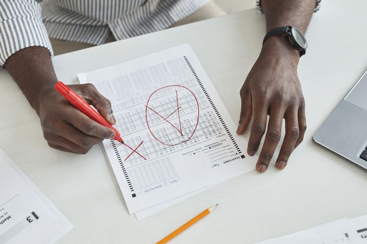 Close-up of a teacher marking a test paper with a red marker on a desk