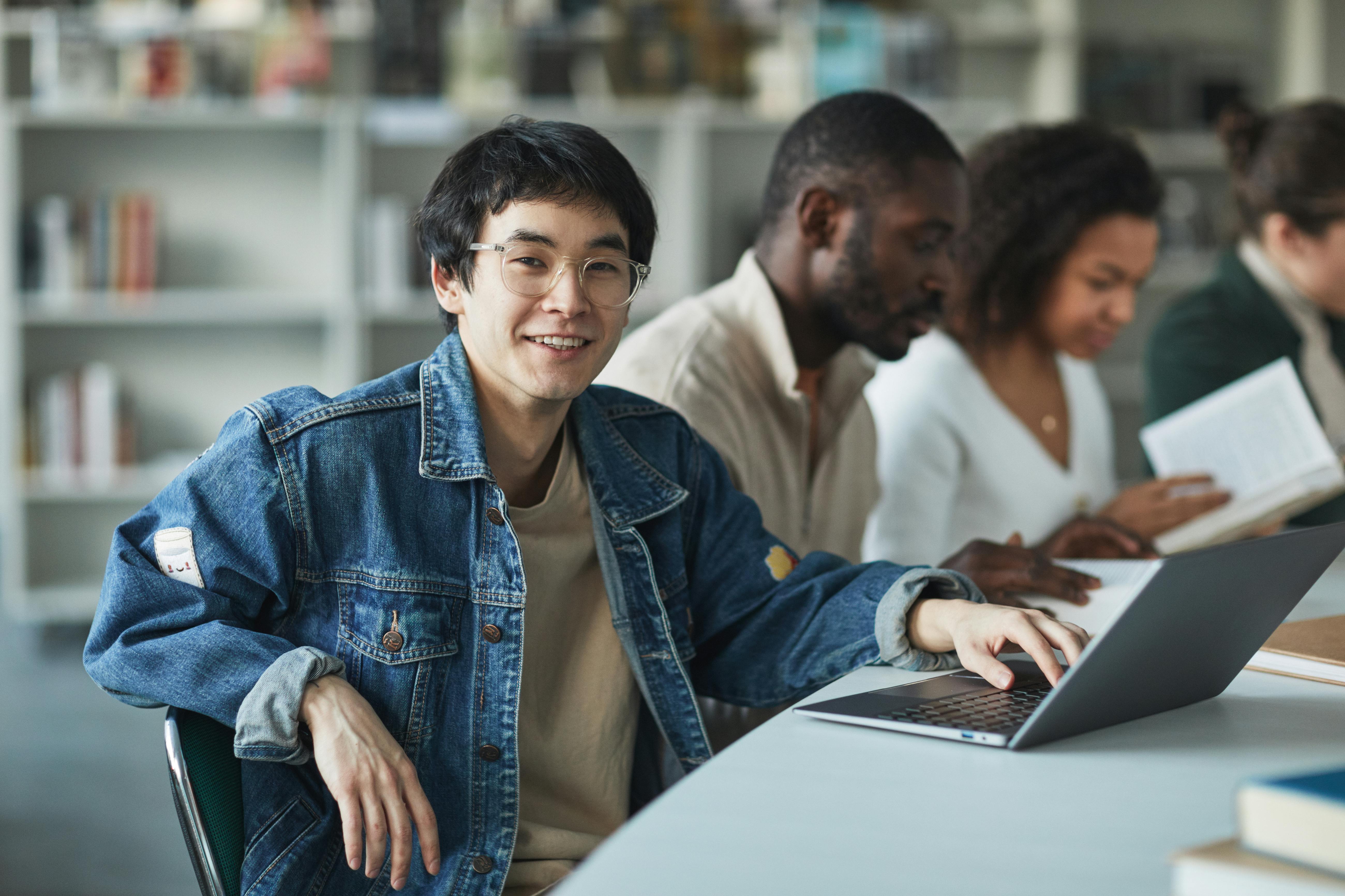 Mahasiswa internasional tersenyum dengan laptop di perpustakaan Australia