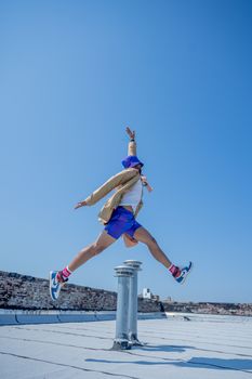 Man in vibrant outfit jumps high on a city rooftop with a clear blue sky backdrop, showcasing freedom and energy.