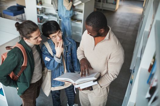 A group of diverse students collaborating over a book in a library setting.