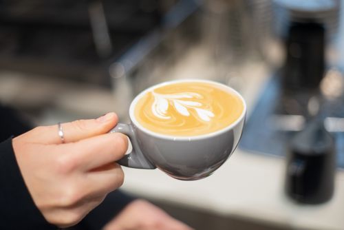 Free Close-up of a hand holding a beautifully crafted latte with latte art in a cozy café. Stock Photo