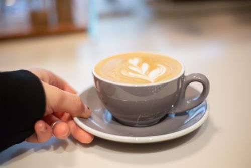 Free Hand holding a cappuccino with latte art in a cozy cafe setting. Perfect warm drink moment. Stock Photo