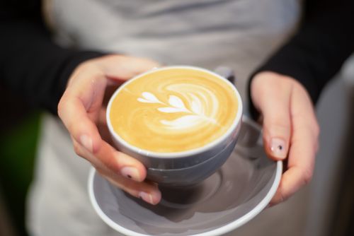Free Close-up of hands holding a cappuccino with intricate latte art, capturing the essence of a cozy cafe moment. Stock Photo