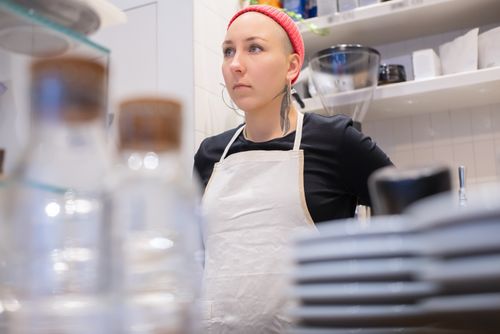 Free Female barista wearing apron and beanie in a stylish coffee shop setting. Stock Photo