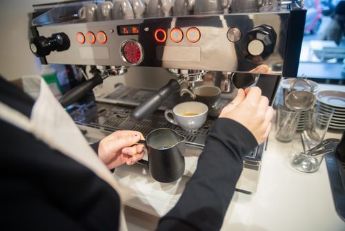 Free A barista prepares an espresso drink using a modern coffee machine in a café setting. Stock Photo
