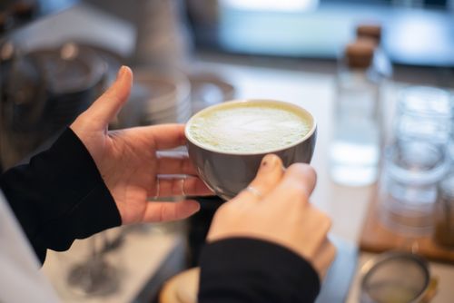 Free A close-up of hands holding a hot matcha latte in a cozy Portugal cafe setting. Stock Photo