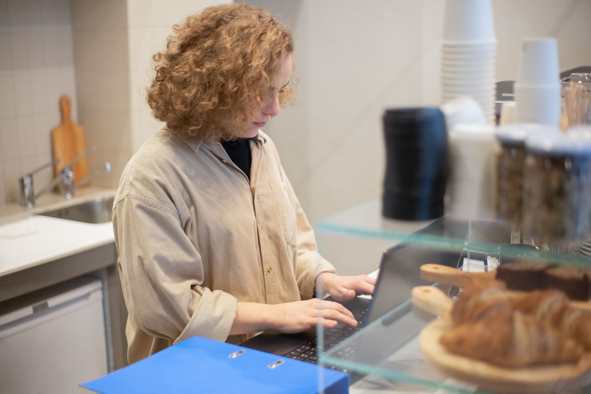 A small business owner working on a laptop behind a cafe counter.