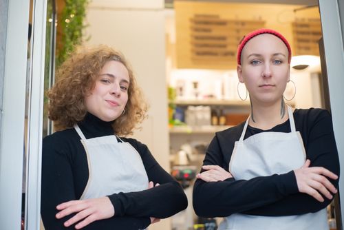 Free Two café employees in aprons posing confidently in the doorway, representing teamwork and professionalism. Stock Photo